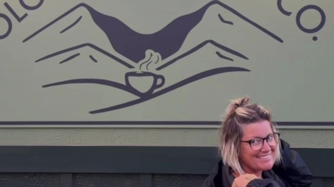 Michelle smiling in front of the painted Olowalu Coffee Co mountain sign.