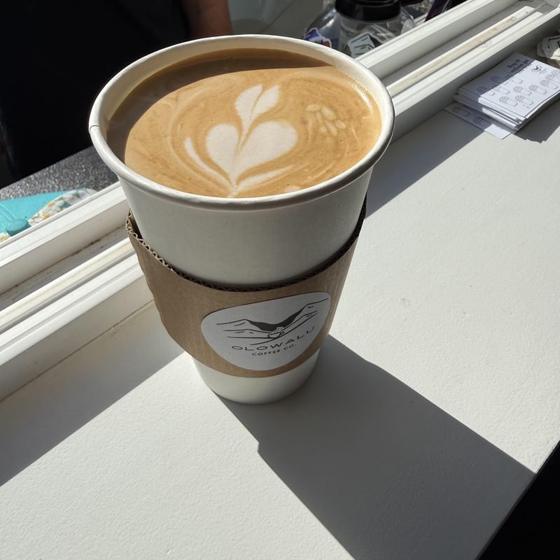A hot latte with latte art in an Olowalu Coffee Co cup on the window ledge.