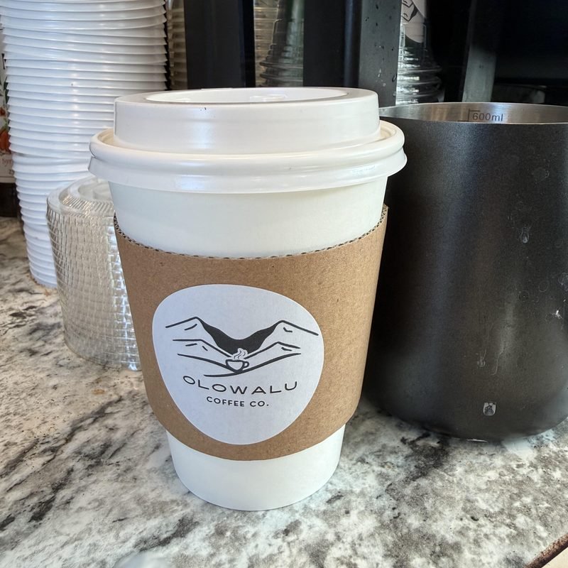 A hot latte in an Olowalu Coffee Co cup with a sleeve, on the counter.