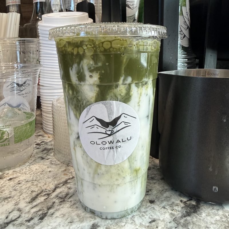 An iced matcha latte in an Olowalu Coffee Co cup on the counter.