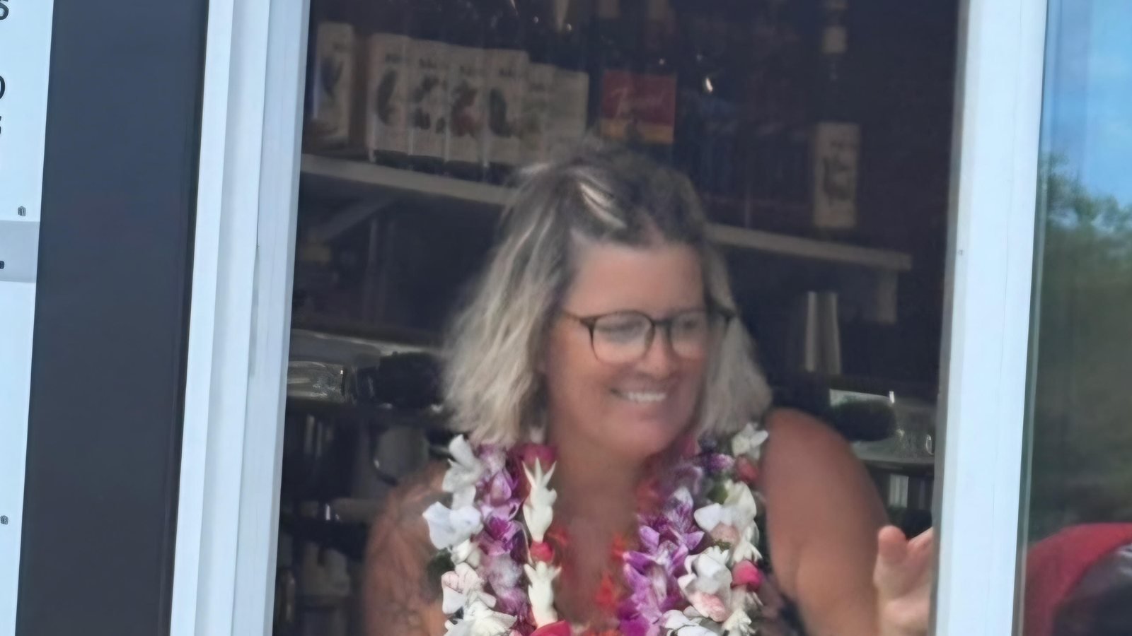 Michelle smiling at the trailer window, wearing flower leis and handing out an iced drink.