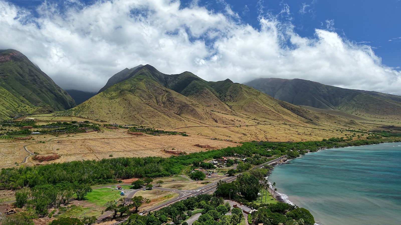 A drone view over the Olowalu coastline and the Honoapiilani Highway, with the Olowalu Coffee Co trailer and the West Maui mountains behind it.